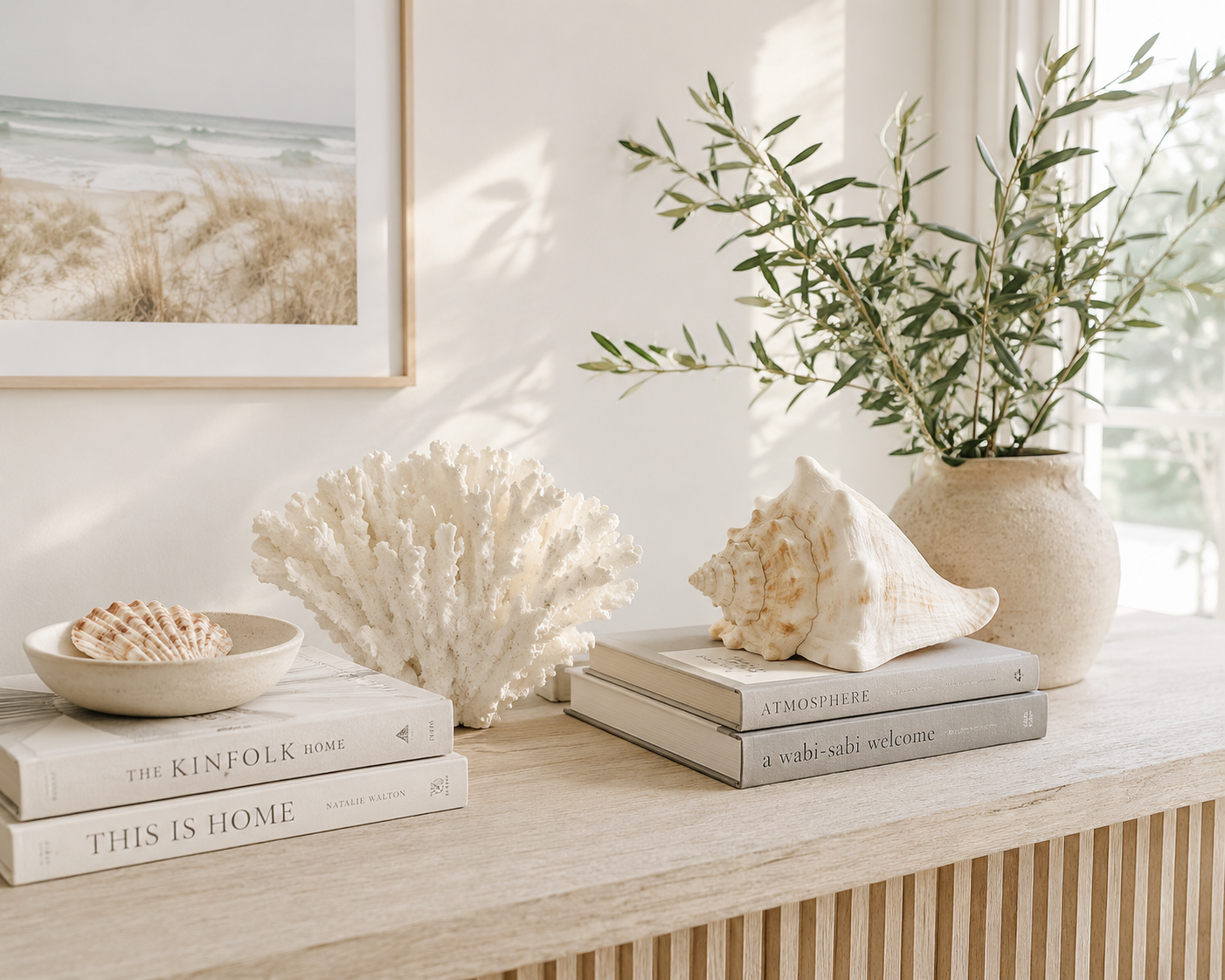 Coastal console styling with shells, white coral, conch shell, stacked books, and olive branches in a ceramic vase